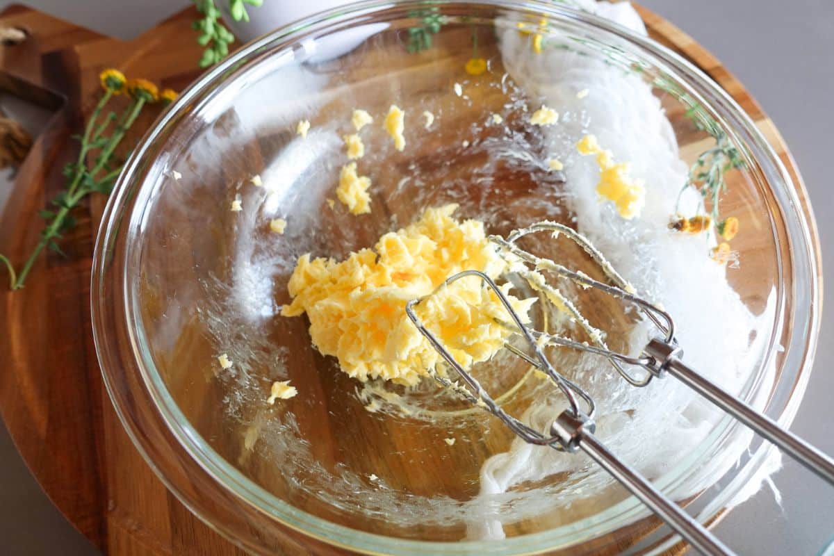 Electric hand mixer beaters in a glass bowl with creamed butter.