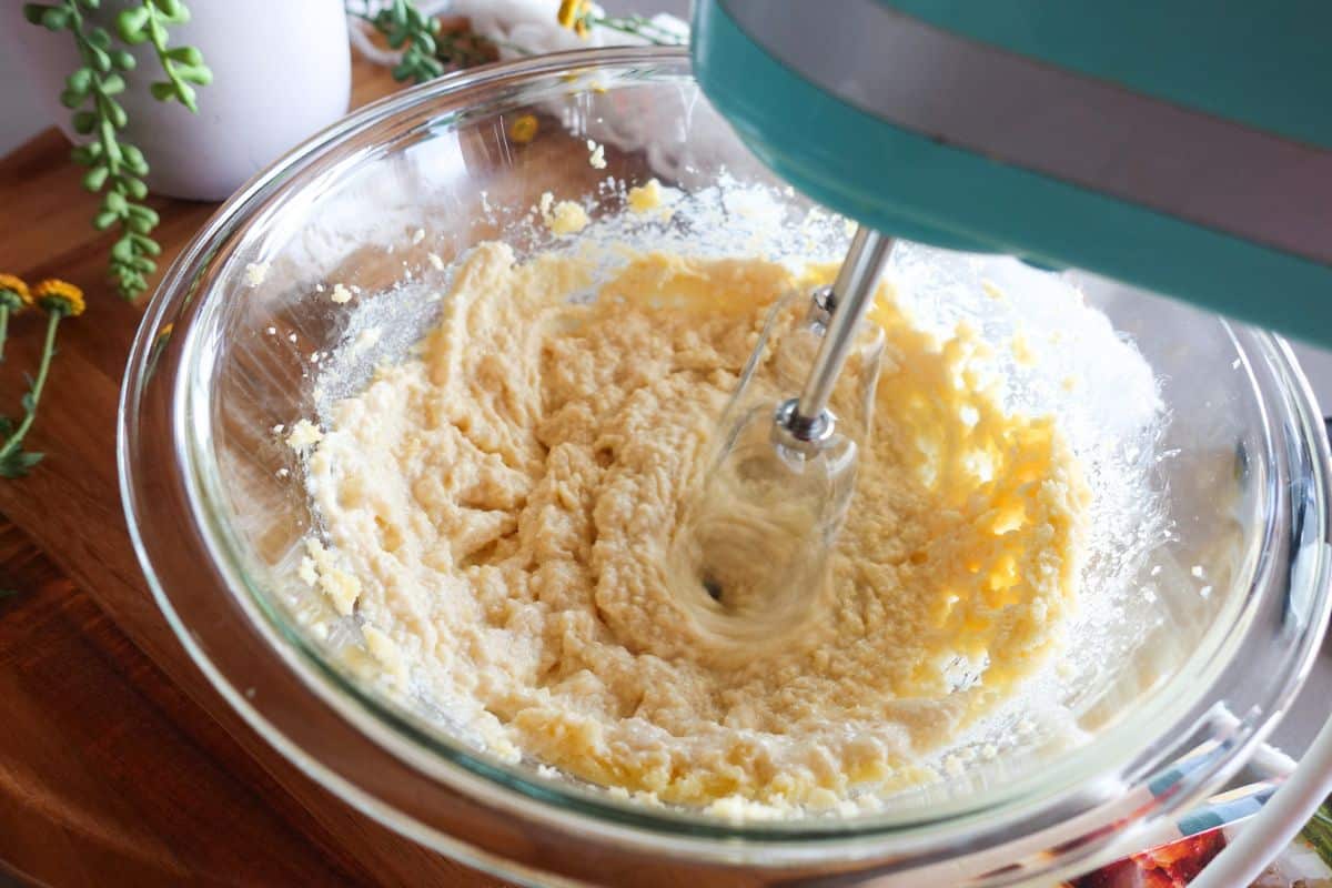 A teal hand mixer blends wet ingredients for cake in a glass bowl.