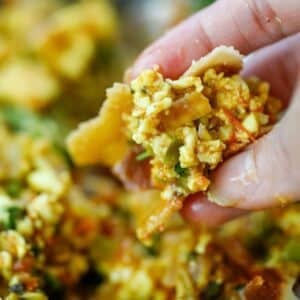 A hand holding a piece of roti topped with Paneer Bhurji and vegetables.