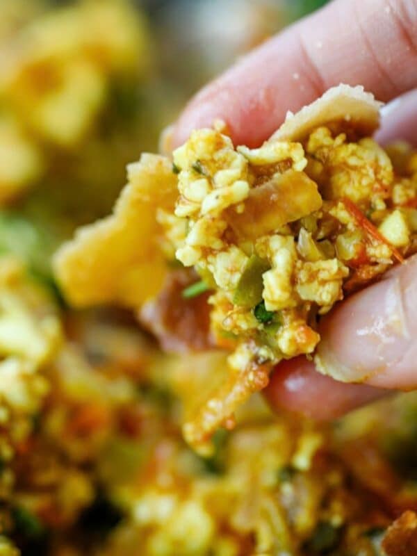 A hand holding a piece of roti topped with Paneer Bhurji and vegetables.