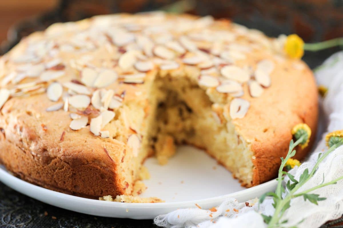 Round almond cake topped with sliced almonds, with one slice removed.